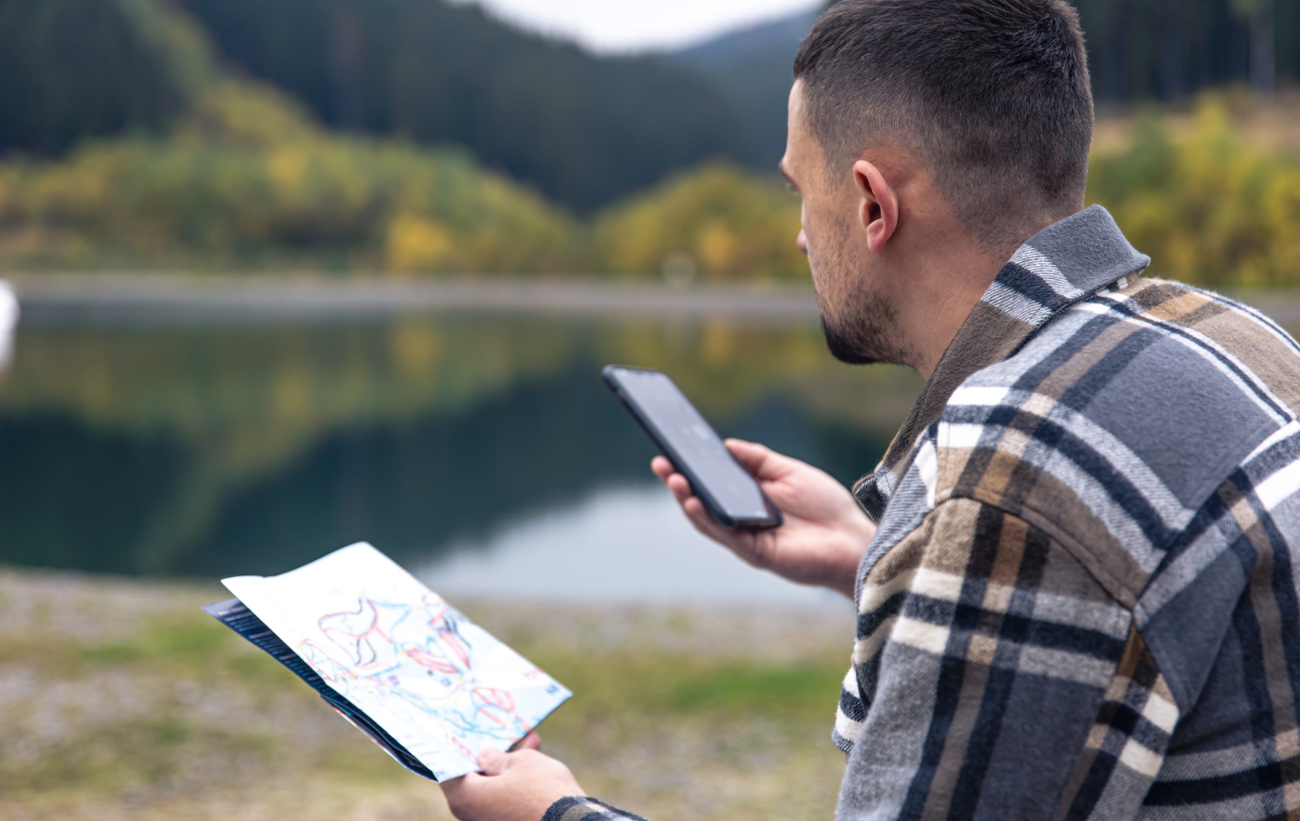 A young man in a plaid shirt with a map and a smartphone in his hands against the backdrop of mountains. img src: freepik